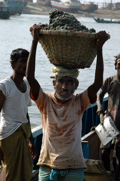 Men carry heavy baskets of sand off the ship