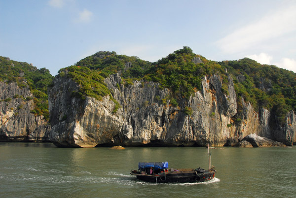 Small cargo vessel crusing by the limestone cliffs of Cat Ba Island