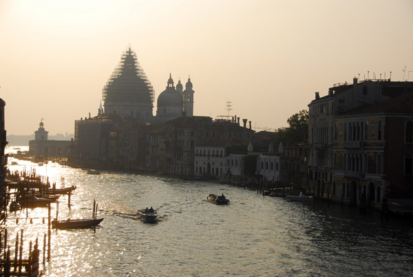 Sun shining on the Grand Canal with a sillhouette of the scaffolding-encrused dome of the Basilica of Santa Maria della Salute