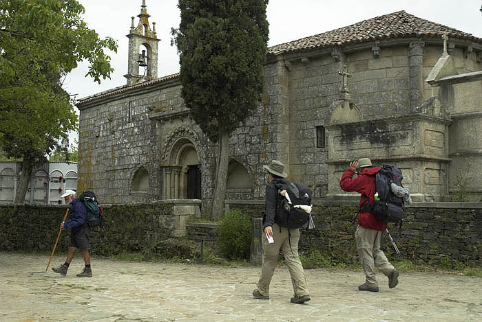 Pilgrims pass a 12th C. church at Melide, Galicia