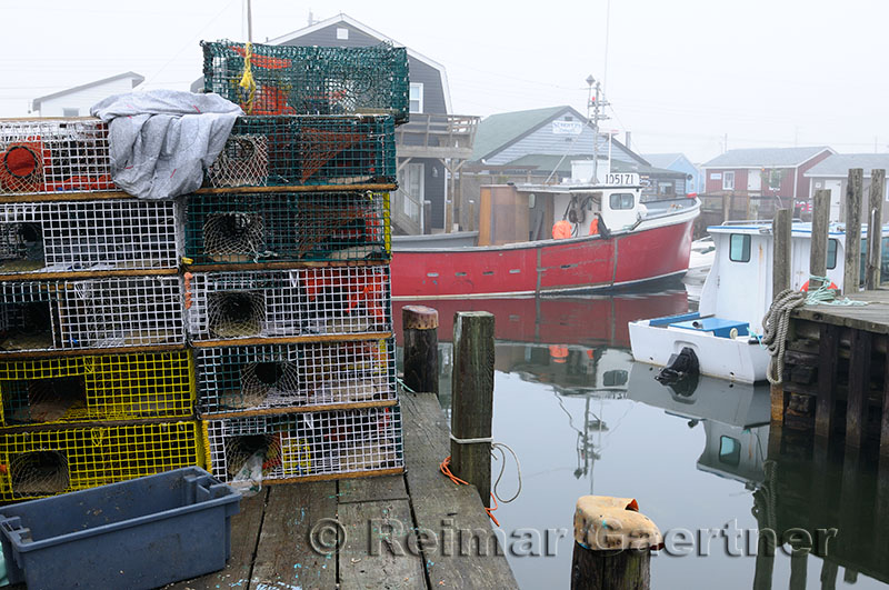 Wire lobster traps on dock and boats in fog at Fishermans Cove Eastern Passage Halifax Nova Scotia