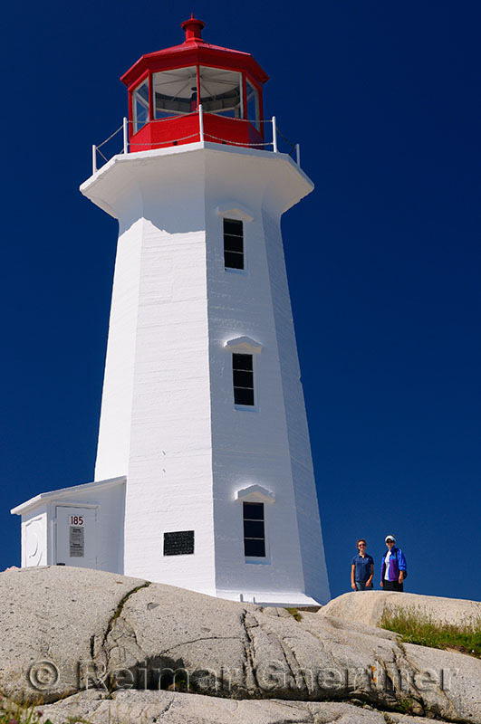 Peggys Cove lighthouse against a blue sky with mother and daughter tourists