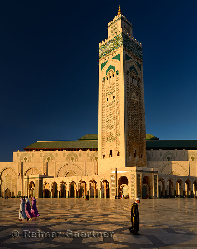 Moroccan man and women walking on the plaza of the Hassan II Mosque Casablanca at sunset