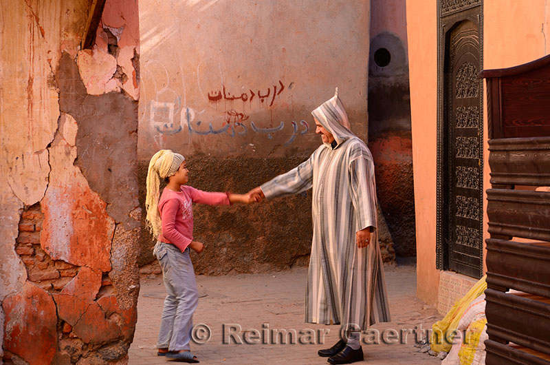 Moroccan man in djellaba greeting a young girl with headscarf in souk of Marrakech