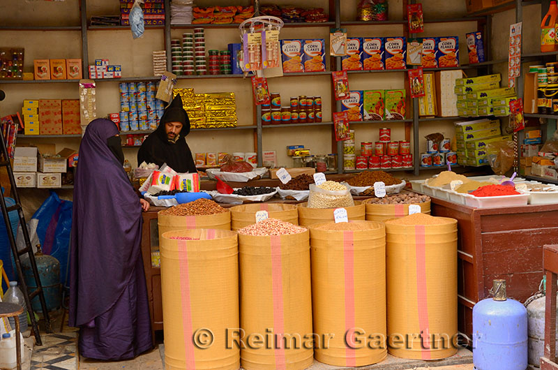 Grocery store worker in djellaba with female customer in purple Hijab in Fes el Bali Medina Morocco