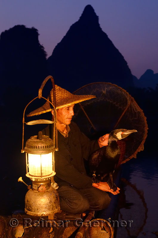 Chinese cormorant fisherman holding his bird at dawn on the Li river Yangshuo China