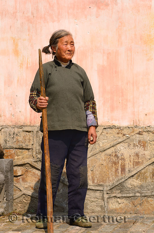 Old Chinese woman with staff standing in ancient village of Chengkan Huangshan China