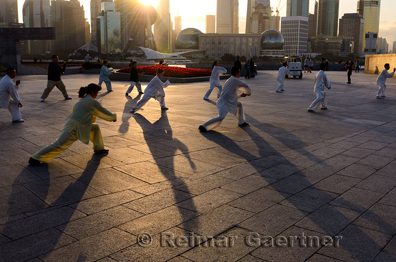 Long shadows of group doing Tai Chi exercises on the Bund at dawn with Shanghai skyline China