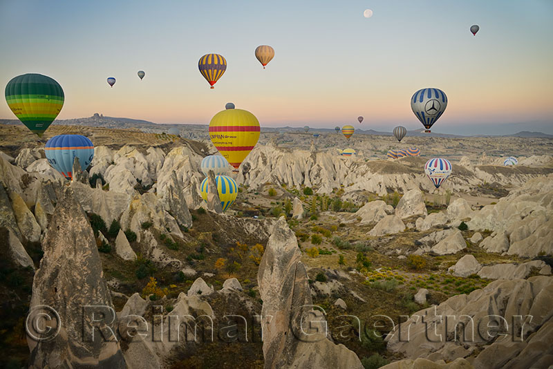 Many hot air balloons over the Red Valley Cappadocia Turkey at dawn with moon