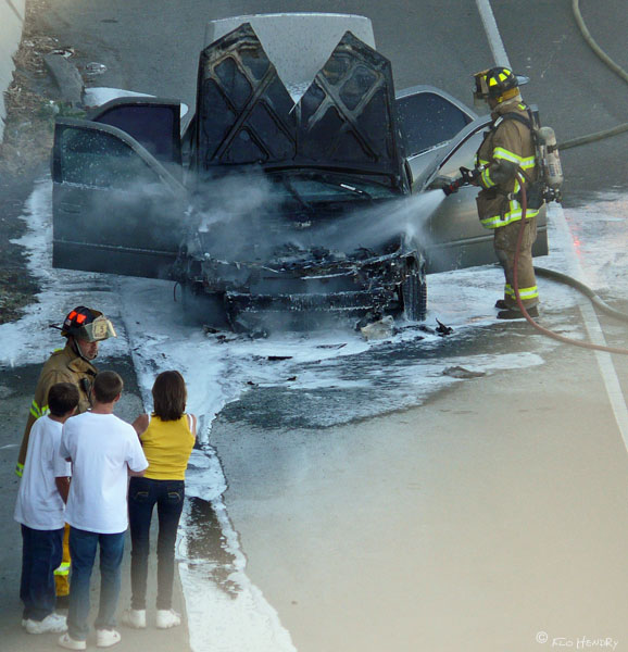 Vehicle Fire [3] One firefighter continues to spray car with water while another talks to the occupants. 