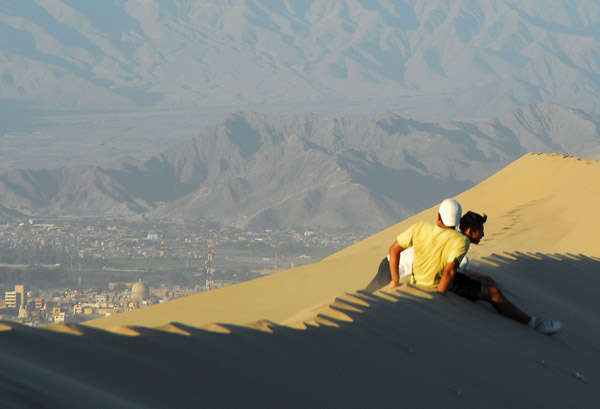 Guys sitting on a dune at Huacachina with Ica in the distance