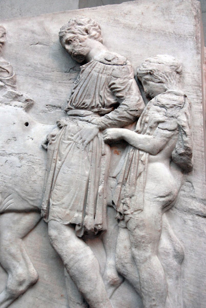 Parthenon North Frieze XLVII figure 135-136, a boy helps a rider adjust the length of his tunic