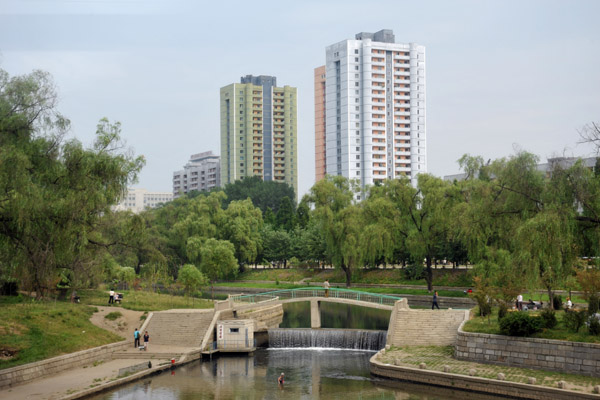 River with a small waterfall and pedestrian bridge, Pyongyang
