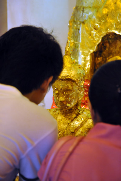 Devout Thais add gold leaf to a Buddha image