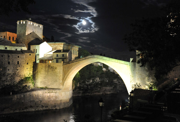 Night view of the Old Bridge of Mostar with a full moon shining through the clouds