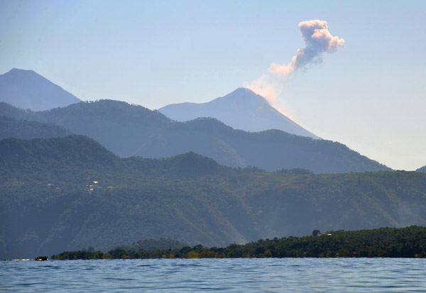 Volcán de Fuego, an active volcano to the east, blows off a puff of ash