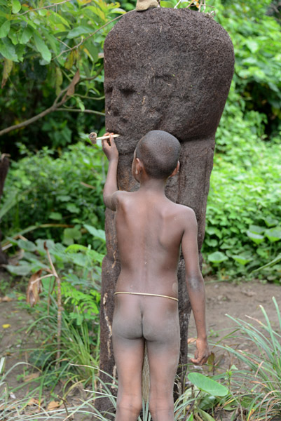The boy places the lit pipe in the mouth of the village idol