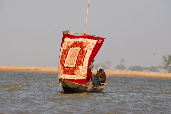 A small boat on the Niger with a colorful sail