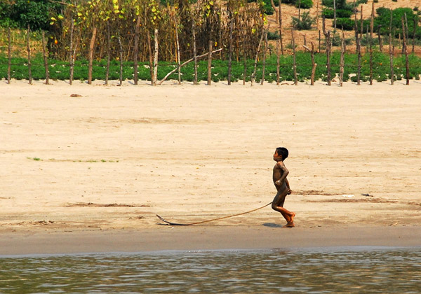 Boy playing with a stick in the mud along the river