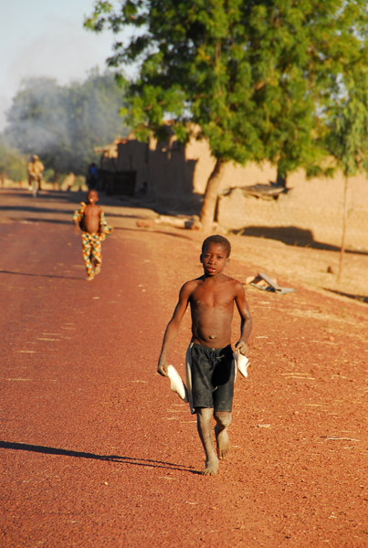 Boy carrying his shoes walking along the road