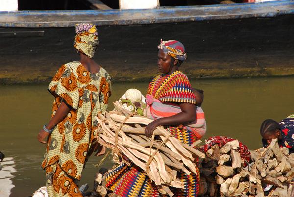 Woman in colorful dress carrying firewood and a baby