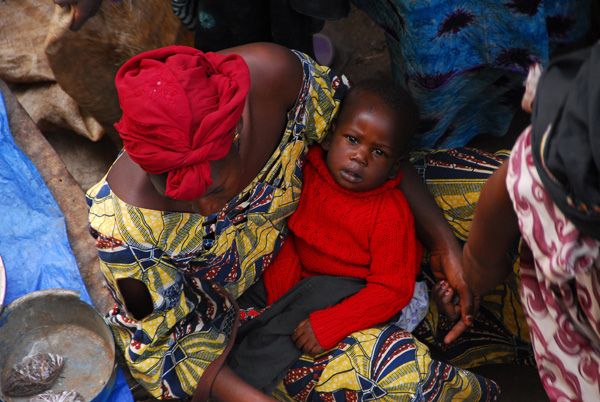 Woman holding a young child while tending a market stall