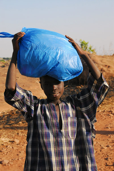 Young man in Félou carrying a large bag on his head