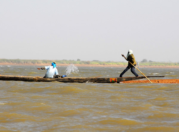 Man puts his weight behind the pole while another bails out the pirogue