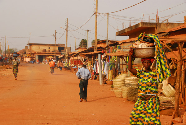 Woman in a colorful dress carrying a load on her head, Abomey
