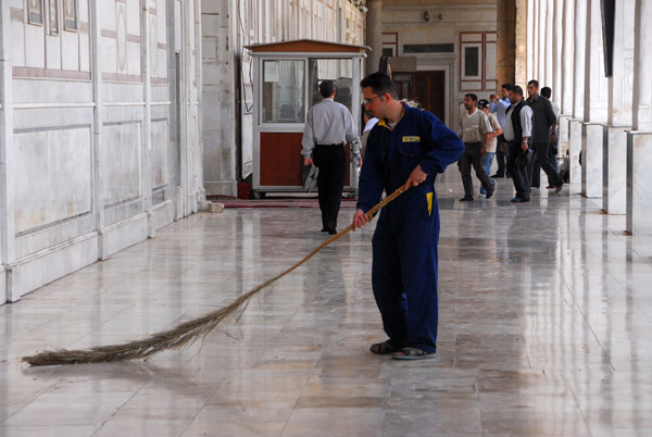 Man sweeping the marble floor with a palm branch