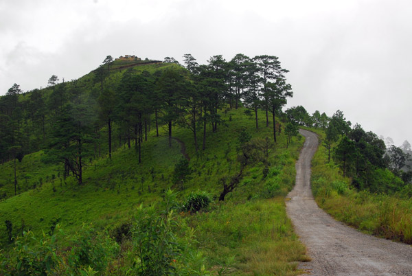 Paved road on the Thai side of the border with a dirt trail on the Myanmar side