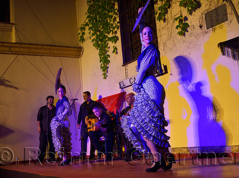 Spotlit female Flamenco dancers on stage with fans and shadows on wall in an outdoor courtyard in Cordoba Spain