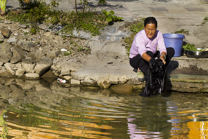 grandma washes cloths by a stream 
