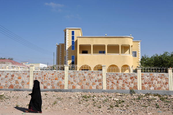 Woman in black passing a villa surrounded by a fancy wall on the edge of Hareisa
