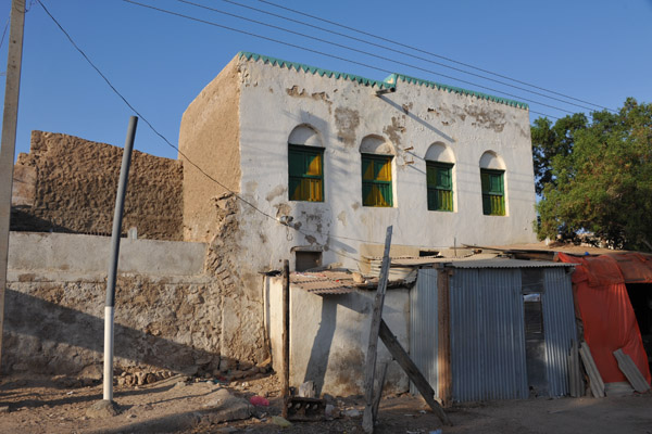 Tin shacks in front of a building with peeling white paint, Berbera