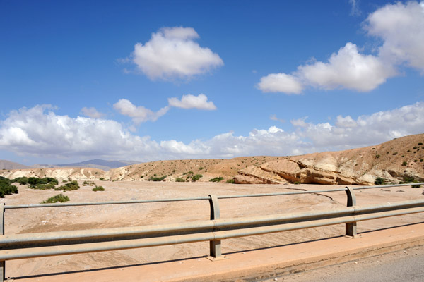 The bridge crosses a broad sandy wadi, a dry riverbed 