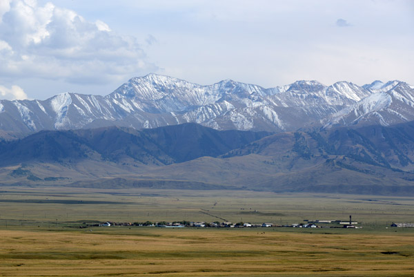 The road climbs giving a view of the grassy plains and snowy mountains