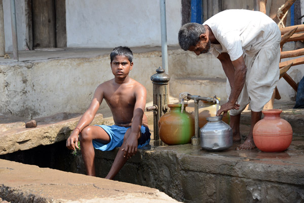 Boy at the town water source as a man fetches water