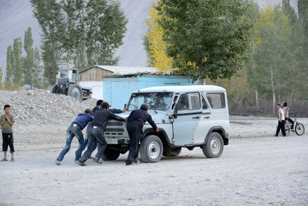 Four men pushing an old Russian 4x4 across the Main Square of Langar