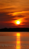 Red ball sunset and reflection from Rocky Harbour Newfoundland with Lobster Cove lighthouse