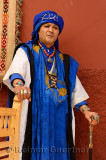 Traditional blue Berber Taureg man standing against a shaded red wall in Marrakech Morocco