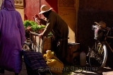 Woman farmer splashing water on her produce in the narrow alley of the souk in Marrakech