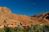 Moon in blue sky over red soil and rock formations in Dades Gorge Morocco