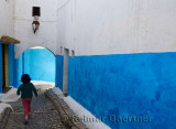 Young girl running along a blue alley of Oudaia Kasbah Rabat Morocco