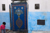 Girl playing at painted blue door in an alley of Oudaia Kasbah Rabat Morocco