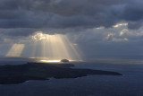 Santorini. Nea Kameni island on the front and the small Aspronissi island under the sun beams