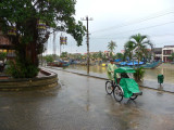 A bicycle rickshaw driver protecting himself from the rain on Bach Dang Street in Hoi An.