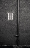 Small White Window by a Crooked Pipe on a Red Wall in a Dark Alley
