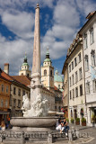 Tourists at the Robba Fountain of the Three Rivers in the Town Square of Ljubljana capitol city of Slovenia with St Nicholas chu
