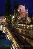 Lights on pink facade of Franciscan Church of the Annunciation and  ballustrades of Triple Bridge over Ljubljanica river Ljublja